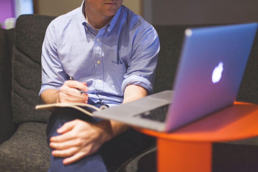 Man taking notes facing Apple Macbook laptop